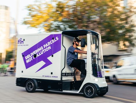 A WHITE AND PURPLE COVERED CARGO BIKE HAS THE FIN LOGO AND THE WORDS DELIVERING PARCELS NOT POLLUTION ON ITS SIDE